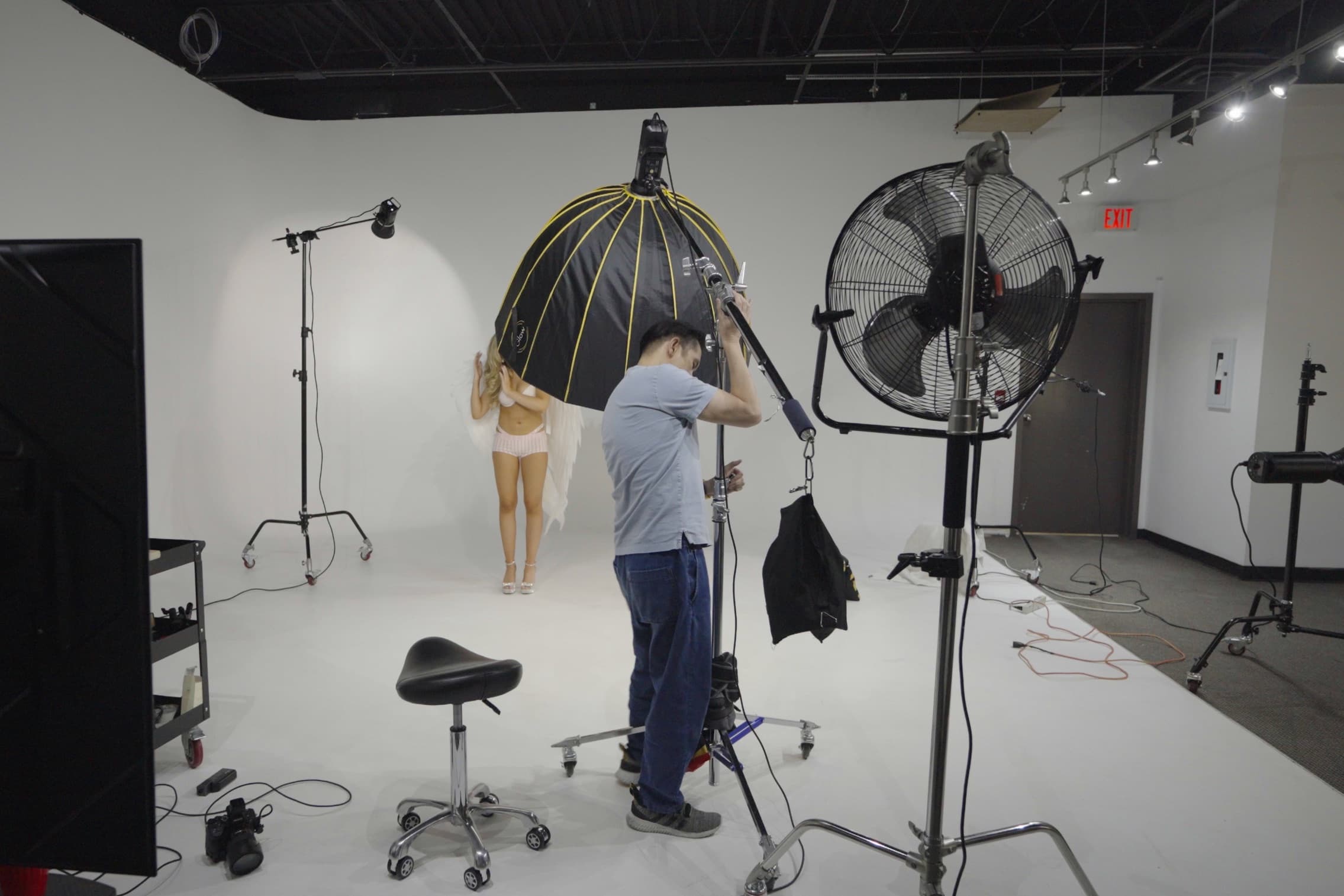 The studio host adjusting a boomed parabolic softbox while the model waits on the cove